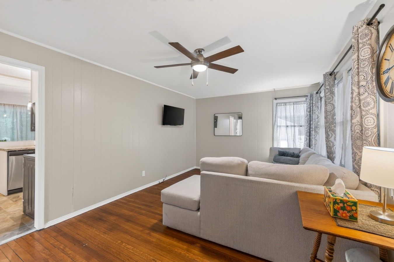 A living room with a ceiling fan, a sofa, a TV, and a dining table with a lamp.