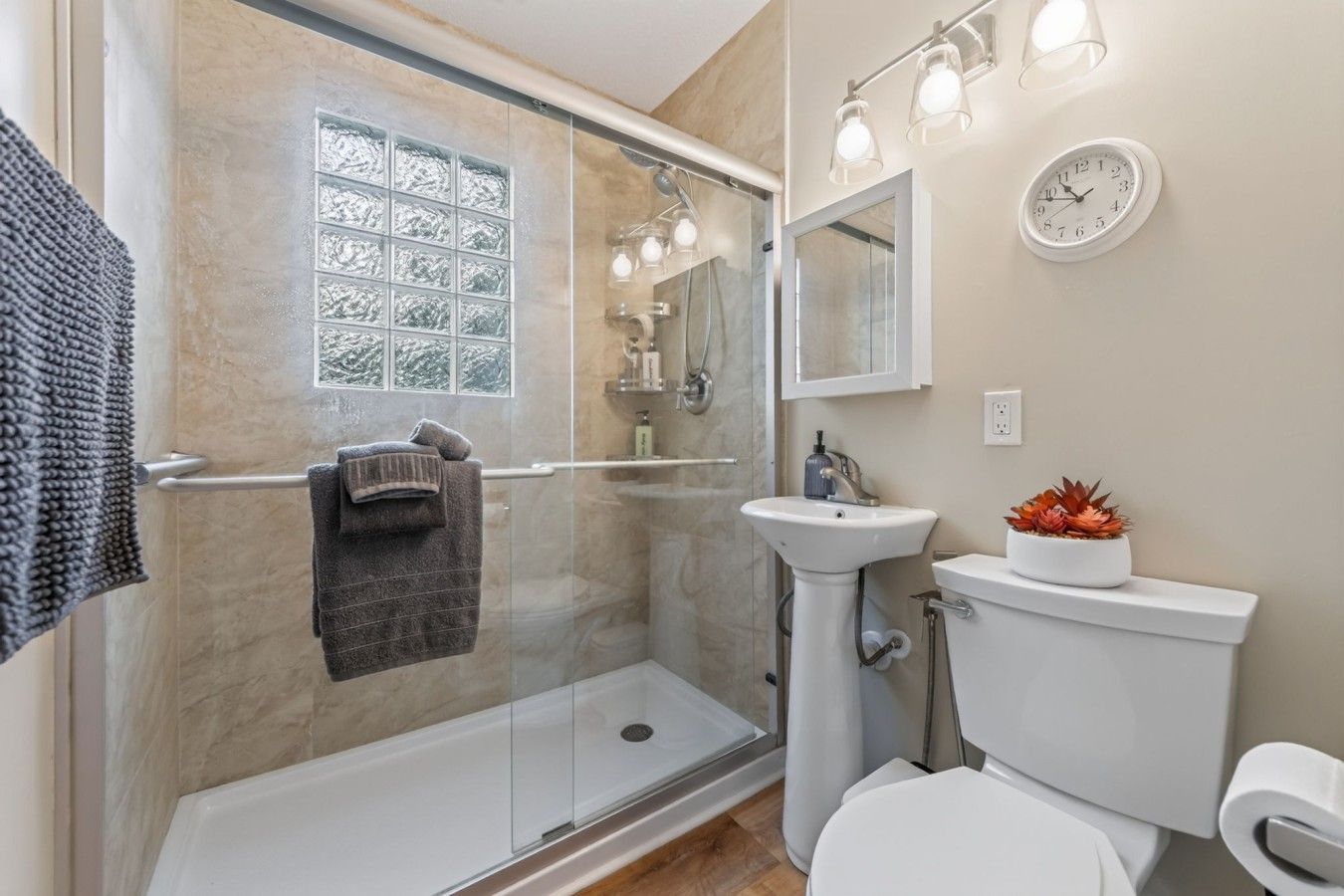 Een moderne badkamer met een douchecabine van glas, een witte wastafel, een toilet en een spiegel.