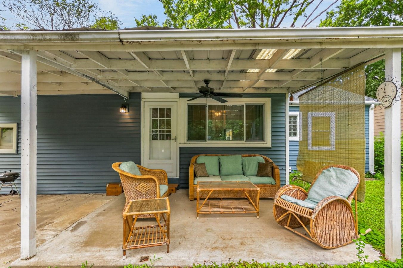 A covered porch with a ceiling fan, a wicker sofa, two wicker chairs, and a small table.