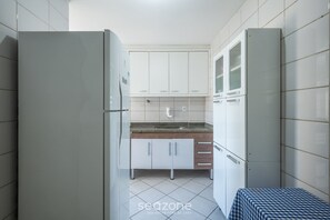 A narrow kitchen with white cabinets, a sink, and a small table with a checkered tablecloth. - 3 Bedroom Apartment 160m From the Beach Dbh0804 (Guarapari)