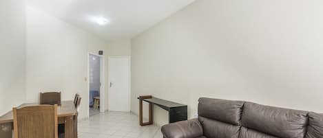 A living room with a brown leather sofa, a wooden dining table with chairs, a small black side table, and a white door leading to another room.
