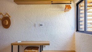 Een kamer met een gestructureerde witte muur, een houten bankje, een klein tafeltje, een geweven mand en een hoed aan de muur.