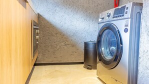 Een kleine wasruimte met een wasmachine, een prullenbak en houten kastjes.