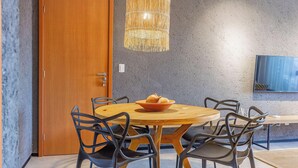 Een eetgedeelte met een ronde houten tafel, zwarte stoelen en een geweven hanglamp.