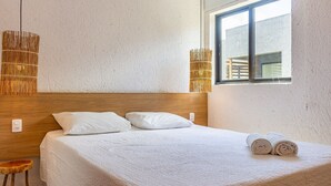 Een keurig opgemaakt bed met witte beddengoed en kussens, een houten hoofdbord en een raam met uitzicht op een gebouw.