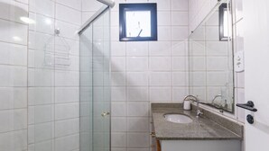 Un baño con cabina de ducha de vidrio, lavamanos con encimera de granito y espejo sobre el lavamanos.