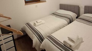 Ett hotellrum med två sängar, ett litet fönster, en takfläkt och en tv som är monterad på väggen.
