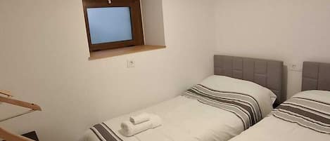 A hotel room with two beds, a small window, a ceiling fan, and a TV mounted on the wall.