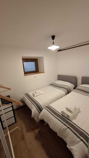 Ein Hotelzimmer mit zwei Betten, einem kleinen Fenster, einem Deckenventilator und einem an der Wand befestigten Fernseher.