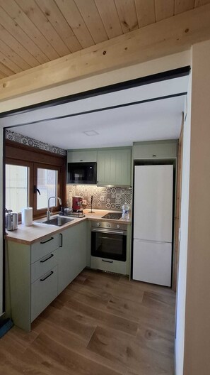 Eine kompakte Küche mit Mikrowelle, Backofen und Kühlschrank. Ein Fenster bietet Blick ins Freie.