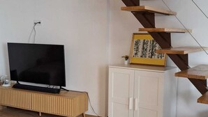 Ett rum med en trätrappa, en platt-TV, ett skåp och ett trägolv.