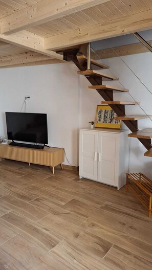 Ein Zimmer mit einer Holztreppe, einem Flachbildfernseher, einem Schrank und Holzboden.