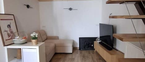 Una sala de estar moderna con piso de madera, un sofá, un televisor y una escalera.