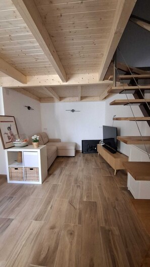 A modern living room with a wooden floor, a sofa, a TV, and a staircase. - La Posada de Cudillero (Cudillero)