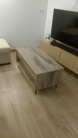 Ein Zimmer mit einem Holztisch, einem Fernseher auf einem Holzschrank und einem hellen Boden.