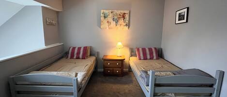 A bedroom with two single beds, a nightstand with a lamp, a framed picture on the wall, and a window.