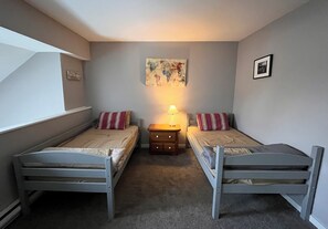 A bedroom with two single beds, a nightstand with a lamp, a framed picture on the wall, and a window.