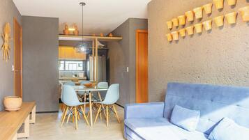 Un salon moderne avec un canapé bleu, un coin repas avec une table et des chaises, et une cuisine en arrière-plan.