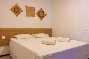Ein ordentlich bezogenes Bett mit weißen Leinen und gerollten Handtüchern, ein Holz-Kopfteil und drei gewebte Wandbehänge.