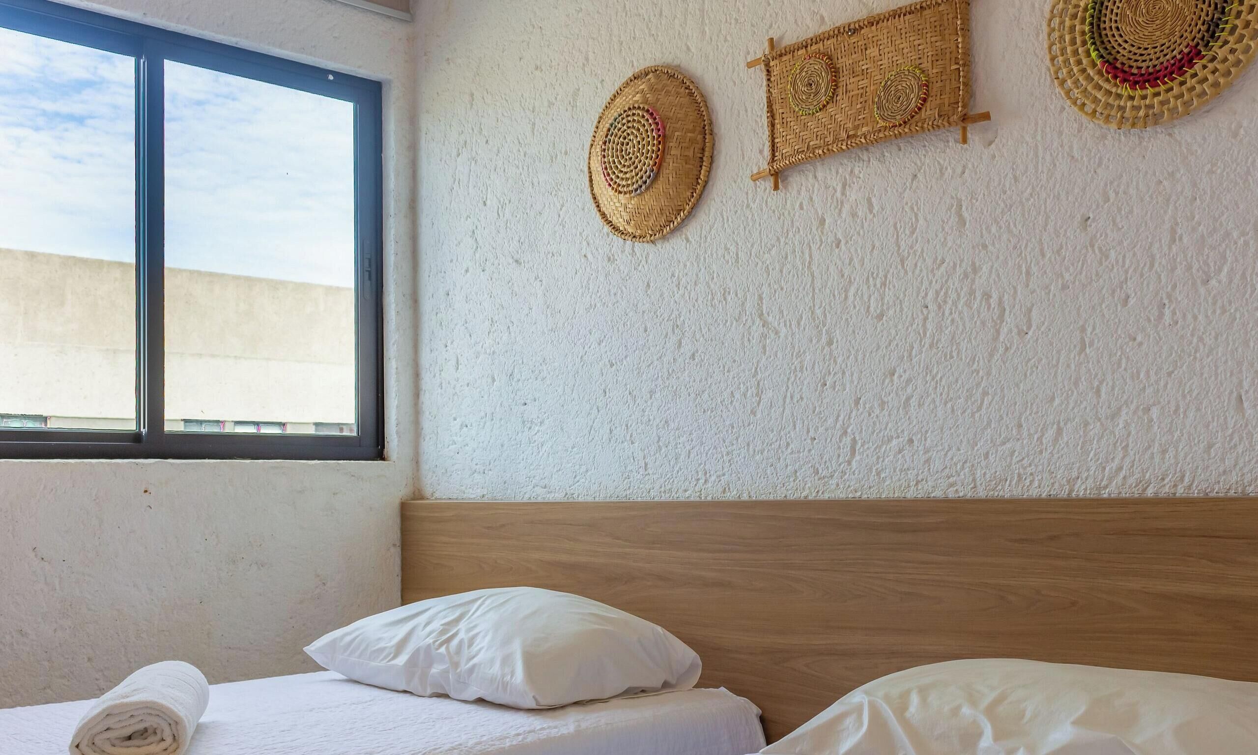 Une chambre à coucher avec un lit, des oreillers, une fenêtre et trois décorations murales tissées.