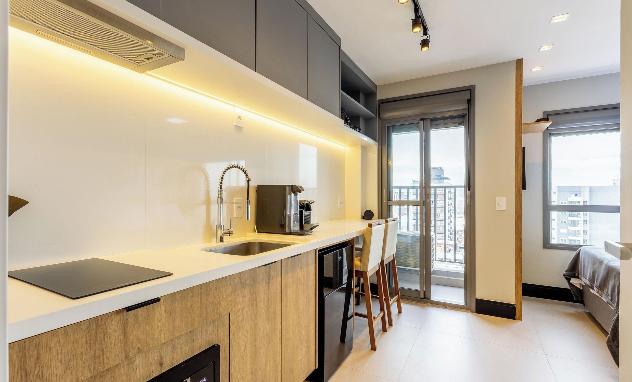 Eine moderne Küche mit Einbauherd, Spüle und Kaffeemaschine. Ein Essbereich mit Tisch und Stühlen lädt zum Verweilen ein, und ein großes Fenster bietet Blick auf die Stadt.