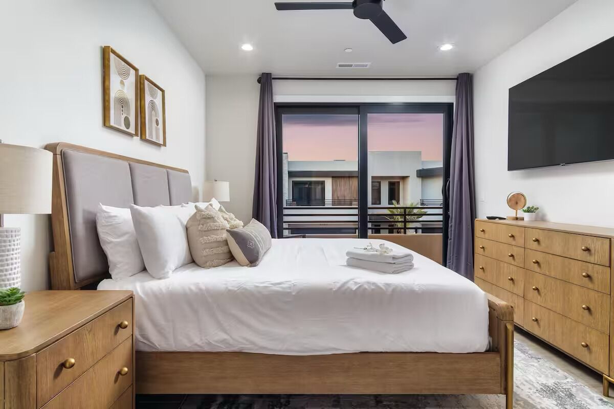 A modern hotel room with a bed, bedside tables, a flat-screen TV, and a large window with a view of the building.