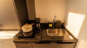 Une petite cuisine équipée d’une cuisinière, d’une machine à café, d’une casserole, d’un évier et d’un petit réfrigérateur.