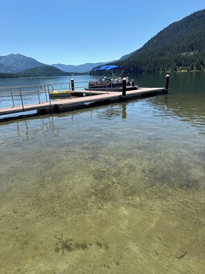 Um lago calmo com um cais que se estende pela água, rodeado por montanhas e floresta.
