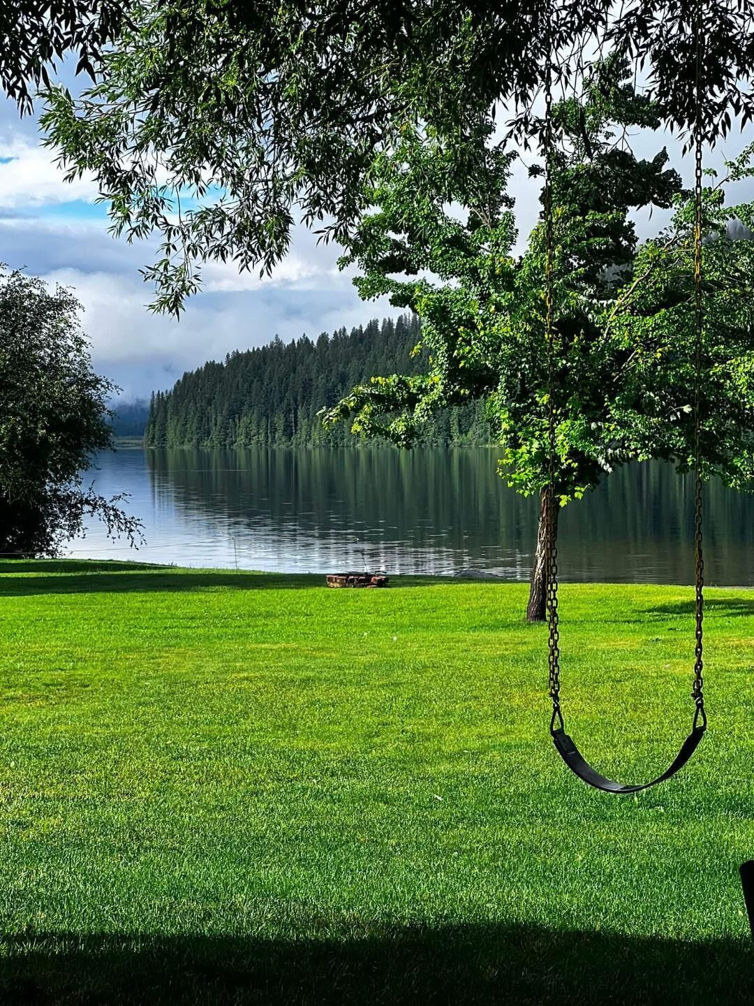 A grassy area with a swing chair and a lake in the background.