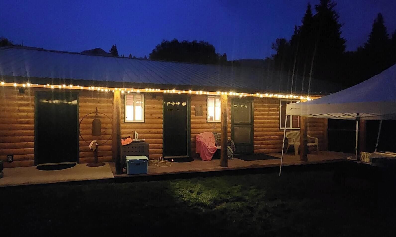 A log cabin with a porch, a small shed, and a covered area with a chair and table.
