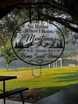 Ein rundes Schild mit Text und einer Berglandschaft, platziert in einem Park mit einer Bank und einem Picknicktisch.