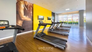 Et fitnessrum med løbebånd, et stort spejl og en gul væg.