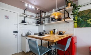 A compact kitchen with white tiled walls, a wooden countertop, and black chairs. There are shelves above the counter holding various kitchen items. - Studio With Heated Pool, at DF Plaza Dpa210 (Águas Claras)