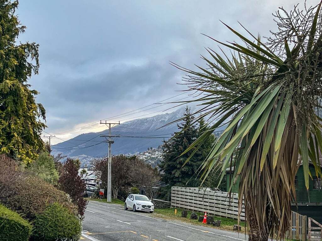 Una carretera con un auto estacionado, una palmera y una montaña al fondo.