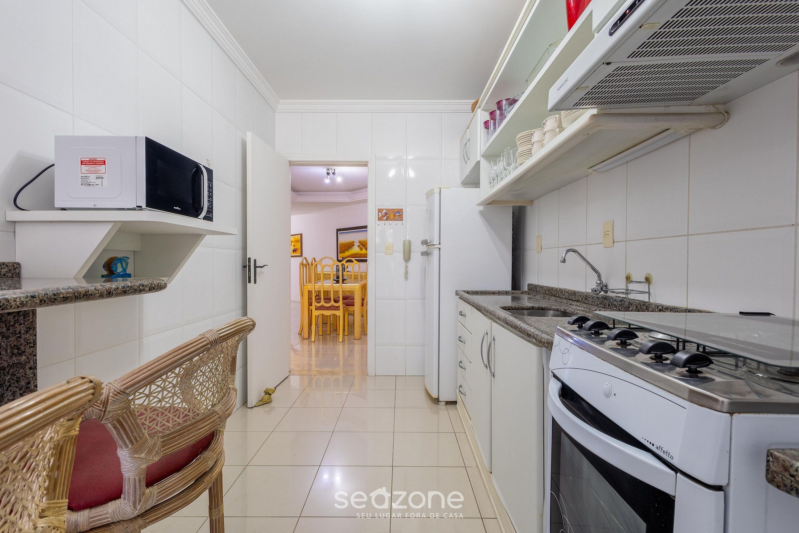 A kitchen with white cabinets, a microwave, a stove, and a dining area with chairs.