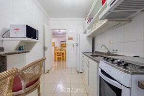 A kitchen with white cabinets, a microwave, a stove, and a dining area with chairs. - Apt Ocean View and Beachfront Dnl0201 (Itapema)