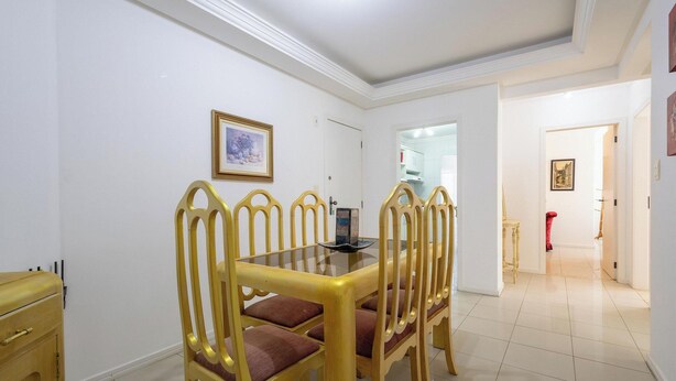 Un comedor con una mesa de vidrio y sillas doradas, una pared blanca con un cuadro enmarcado, y un pasillo que conduce a otra habitación.