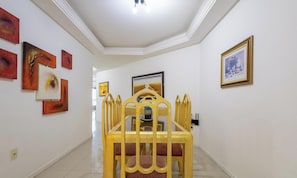 Un pasillo con una silla amarilla, obras de arte enmarcadas en las paredes e iluminación empotrada en el techo.