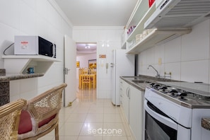 Una cocina con armarios blancos, microondas, estufa y un comedor con sillas.
