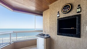 Un balcón con vista a la playa, un lavamanos pequeño y una zona de parrilla con un reloj y botellas.