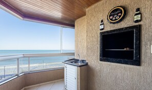 Un balcón con vista a la playa, un lavamanos pequeño y una zona de parrilla con un reloj y botellas.