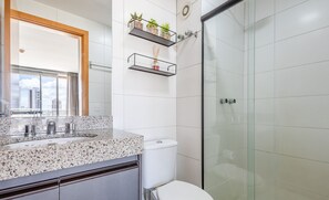 Uma casa de banho moderna com bancada de granito, sanita e cabine de duche em vidro.