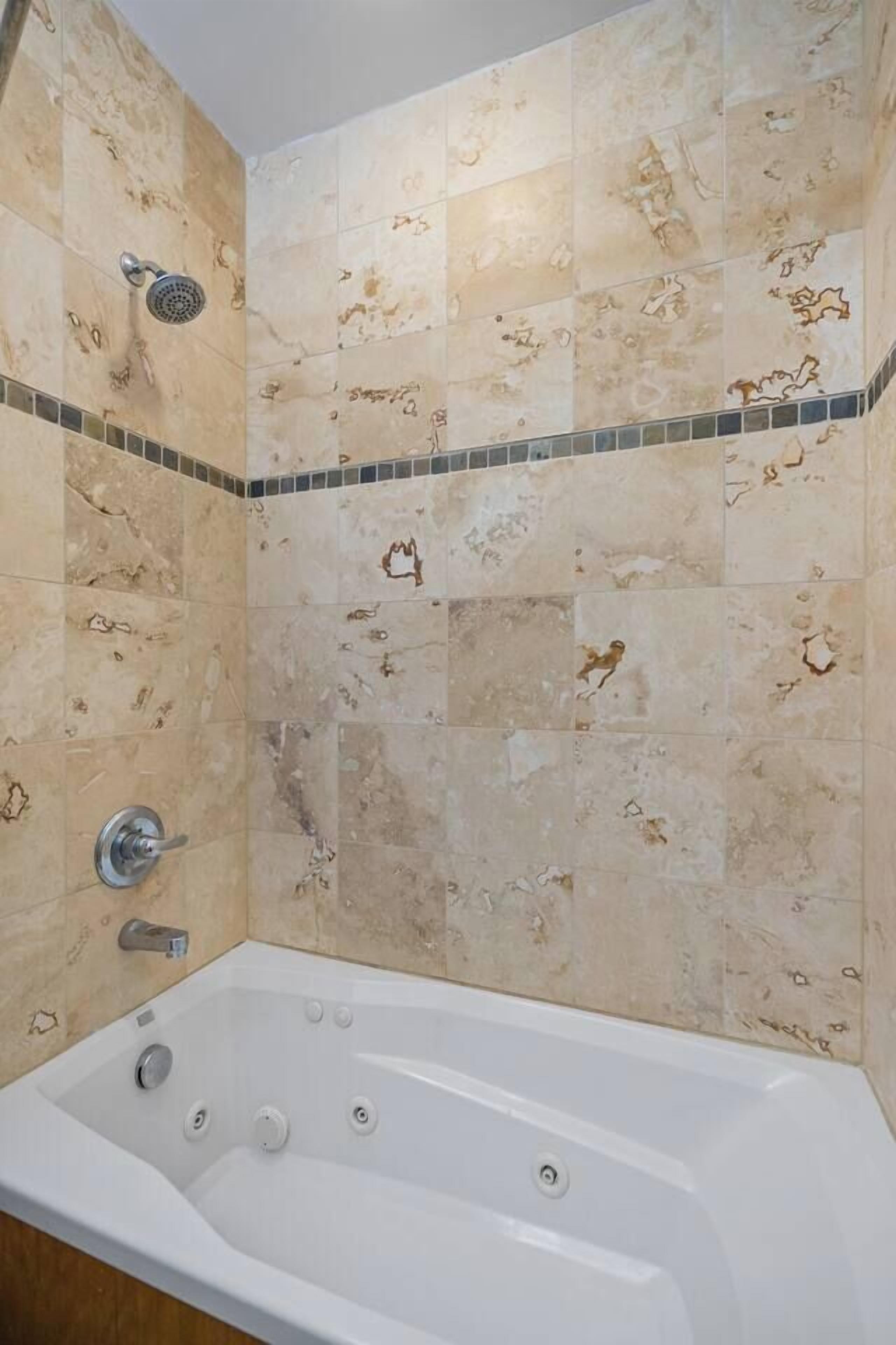 Un baño con una bañera independiente, un cabezal de ducha y un revestimiento de azulejos con un detalle decorativo.