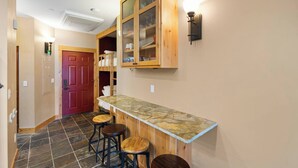 A kitchen with a stone countertop, wooden bar stools, a red door, and a cabinet with glass doors. - Alpine Suite, Sauna, Pool Table & DT Kellogg (Kellogg)
