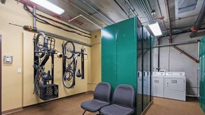 A room with two patterned chairs, a wall-mounted bicycle rack, and a laundry area with dryers. - Alpine Suite, Sauna, Pool Table & DT Kellogg (Kellogg)