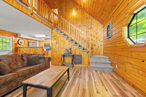 A wooden interior with a staircase, a sofa, a table, and a window. - Marvelous 2-bedroom cabin located behind Dollywood. (Sevierville)