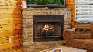 A stone fireplace with a fire, a television mounted above it, and a wooden wall. - Marvelous 2-bedroom cabin located behind Dollywood. (Sevierville)