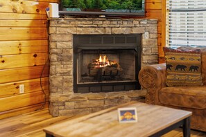 Ein Kamin aus Stein mit Feuer, ein darüber montierter Fernseher und eine Holzwand.