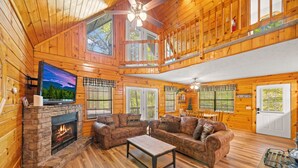 A log cabin interior with a stone fireplace, leather couches, a dining area, and a balcony. - Marvelous 2-bedroom cabin located behind Dollywood. (Sevierville)