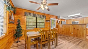 A wooden interior with a dining table, chairs, a ceiling fan, and a kitchen area. - Marvelous 2-bedroom cabin located behind Dollywood. (Sevierville)